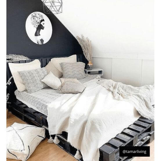 Gezellige slaapkamer met Marokkaanse pompomdeken in crème op een houten paletbed, omgeven door stijlvolle decoraties.