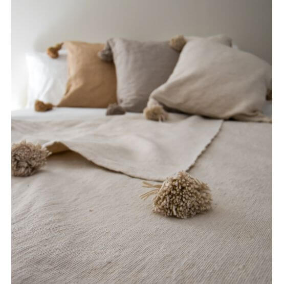Alt Tag: Crème Marokkaanse pompomdeken op bed met kussens, perfect voor modern en bohemien interieur.