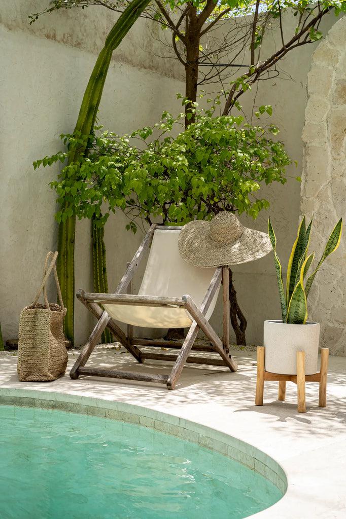 Boho tuin met houten stoel, plant in pot en zwembad bij tropisch groen. Perfecte zomerse rustplek buiten.