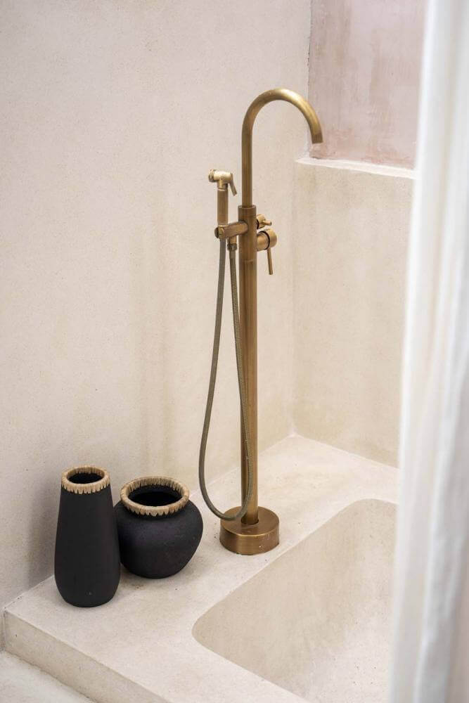 Elegant badkamerhoekje met zwarte, boho vazen en stijlvolle gouden kraan op een crèmekleurige ondergrond.