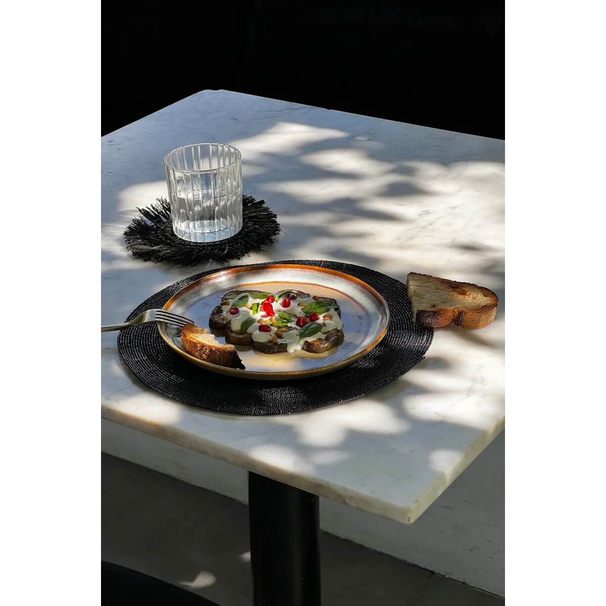 Bohemian chic table setting with De Beaded Placemat in zwart color, featuring a stylish dish on a marble table.