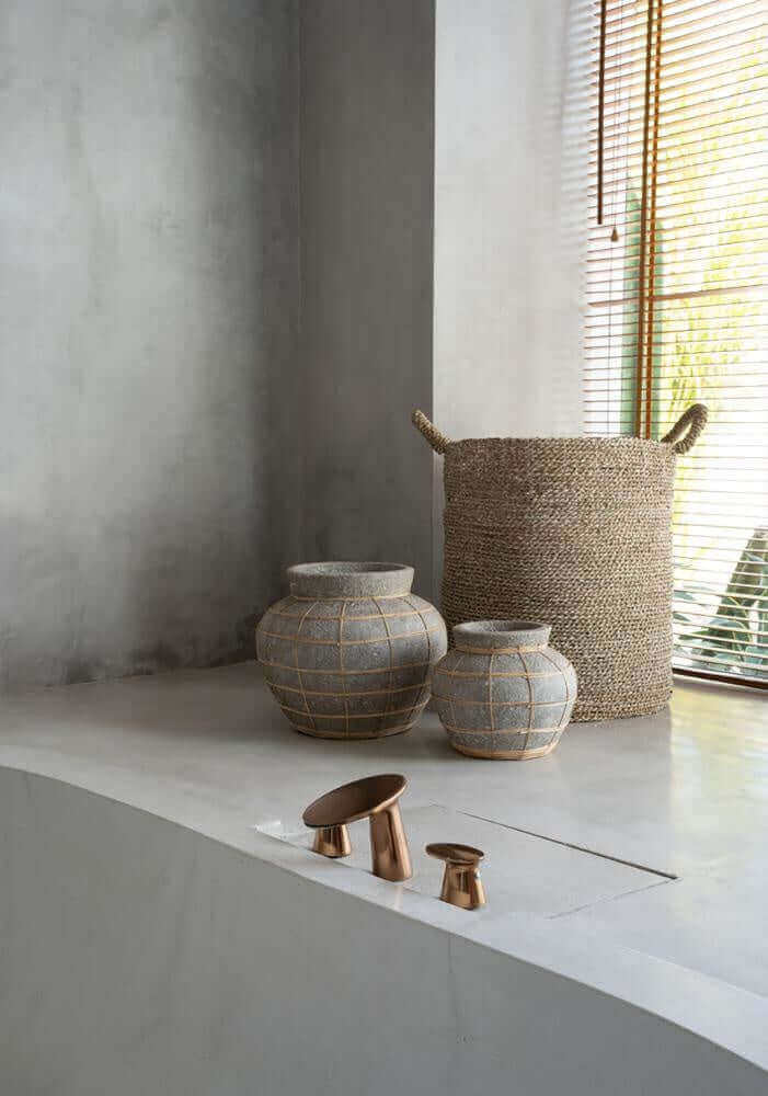Stijlvolle De Belly Vaas van terracotta met rotan detail, in een moderne interieursetting met beton natuurlijke kleuren.