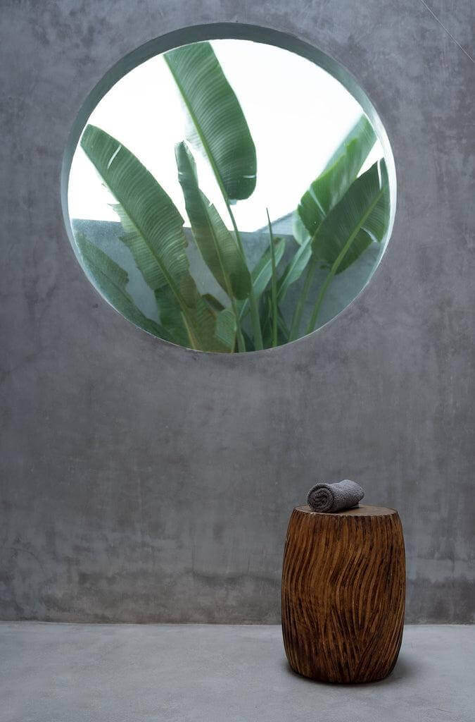 De Celebes Kruk van suarhout, met boomring houtsnijwerk, staat voor een rond raam met planten, voor een natuurlijke sfeer.