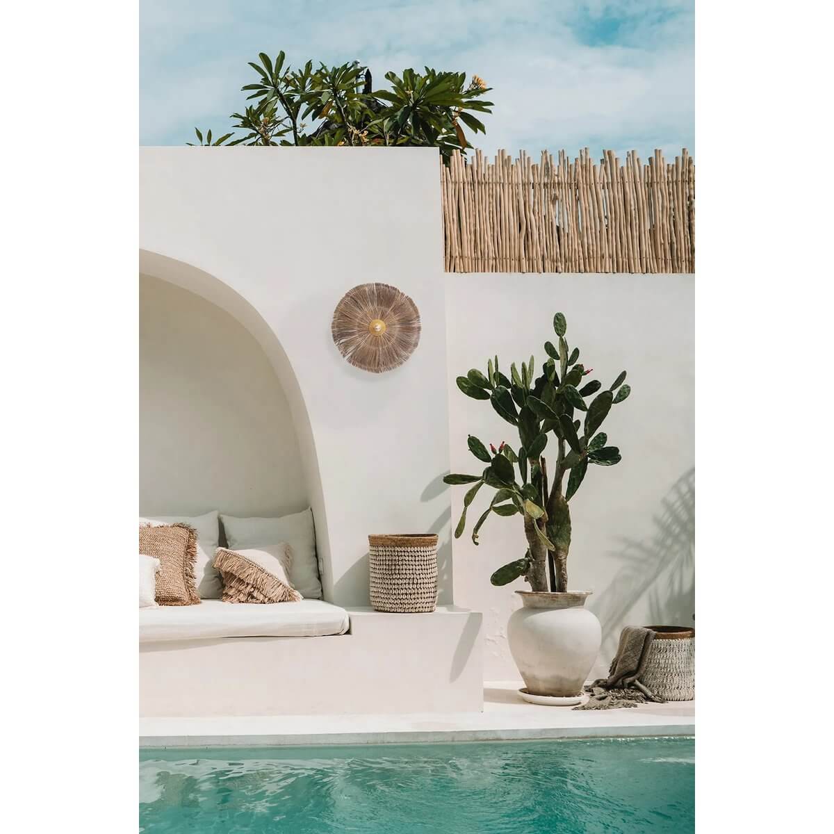 Stijlvolle Chi-Chi wandlamp in natuurlijk messing op een moderne patio met zwembad, lage witte muur en tropische planten.