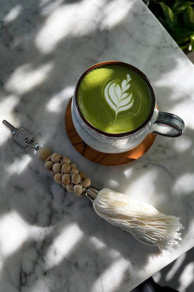 Groene latte en decoratieve sleutelhanger op marmeren tafel.