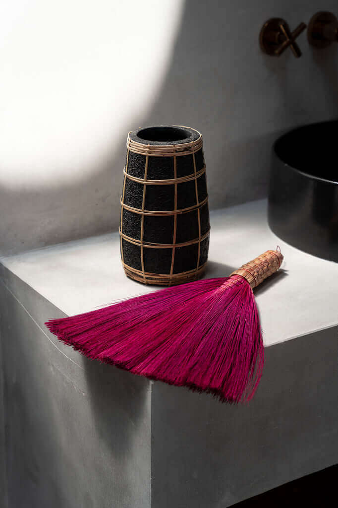 Stijlvolle De Cutie Vaas in zwart met rotan detail en roze borstel op grijze tafel, perfecte decoratie voor een rustieke sfeer.