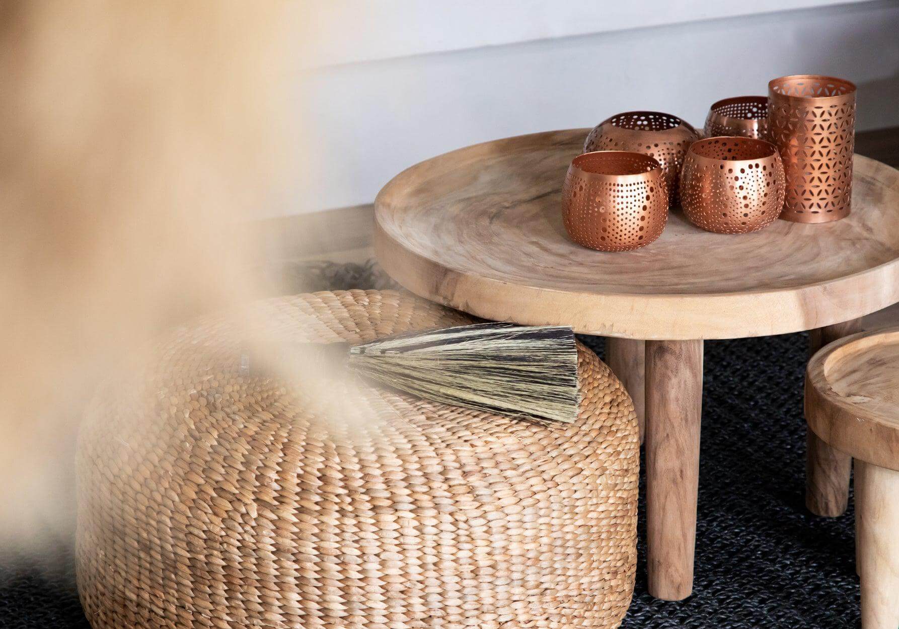 Boho poef en houten tafel met koperen decoraties voor een natuurlijke sfeer in interieur of tuin.
