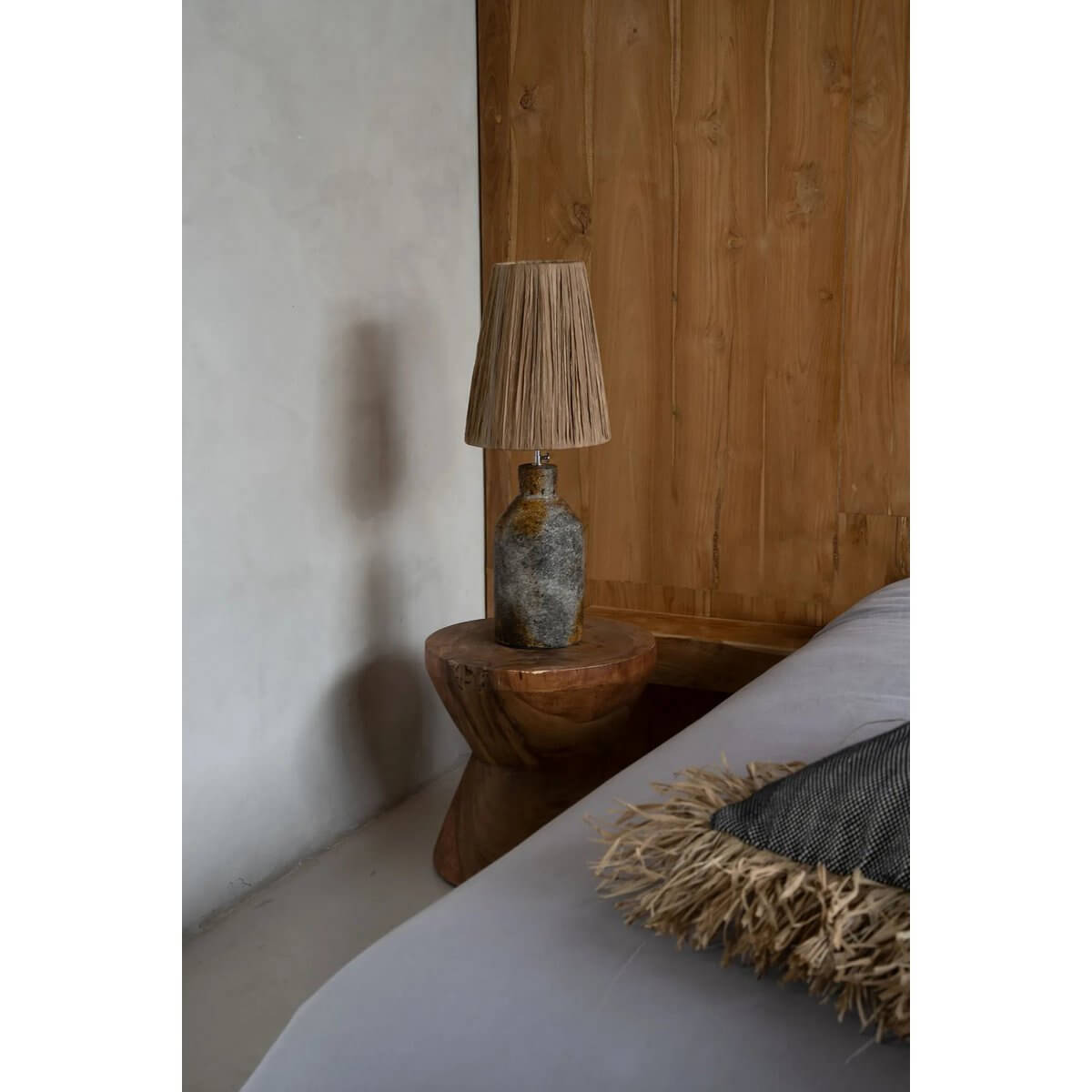 De Ithaka Bohemian tafellamp met terracotta basis en gras lampenkap, antiek grijs natuurlook, op houten tafel naast bed.