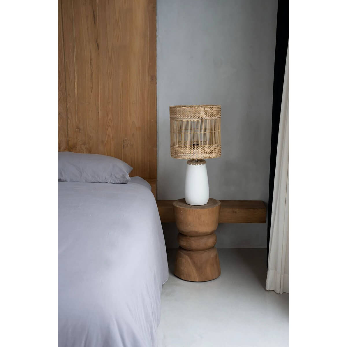 Bohemian white terracotta and rattan table lamp beside a bed in a modern bedroom.