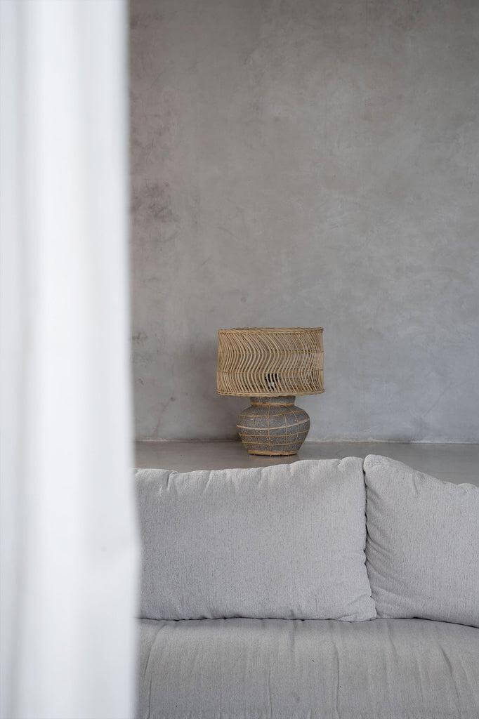 Gezellige De Kythira tafellamp met rotan en terracotta op grijze bank, perfect voor nachtkastje of console.