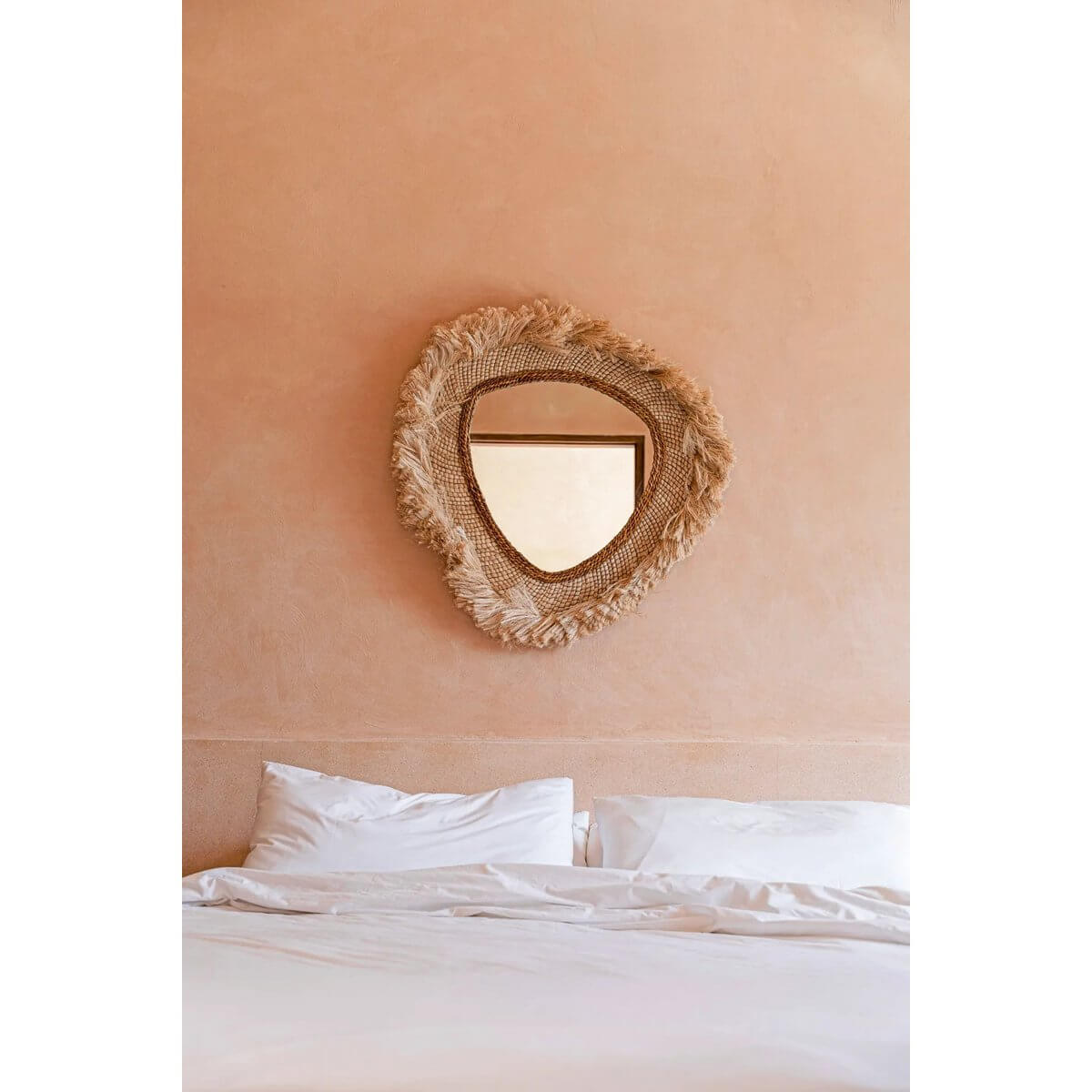 De La Contessa Spiegel tegen een zachte roze muur boven een bed, met een elegant gebogen, natuurlijk houten frame.