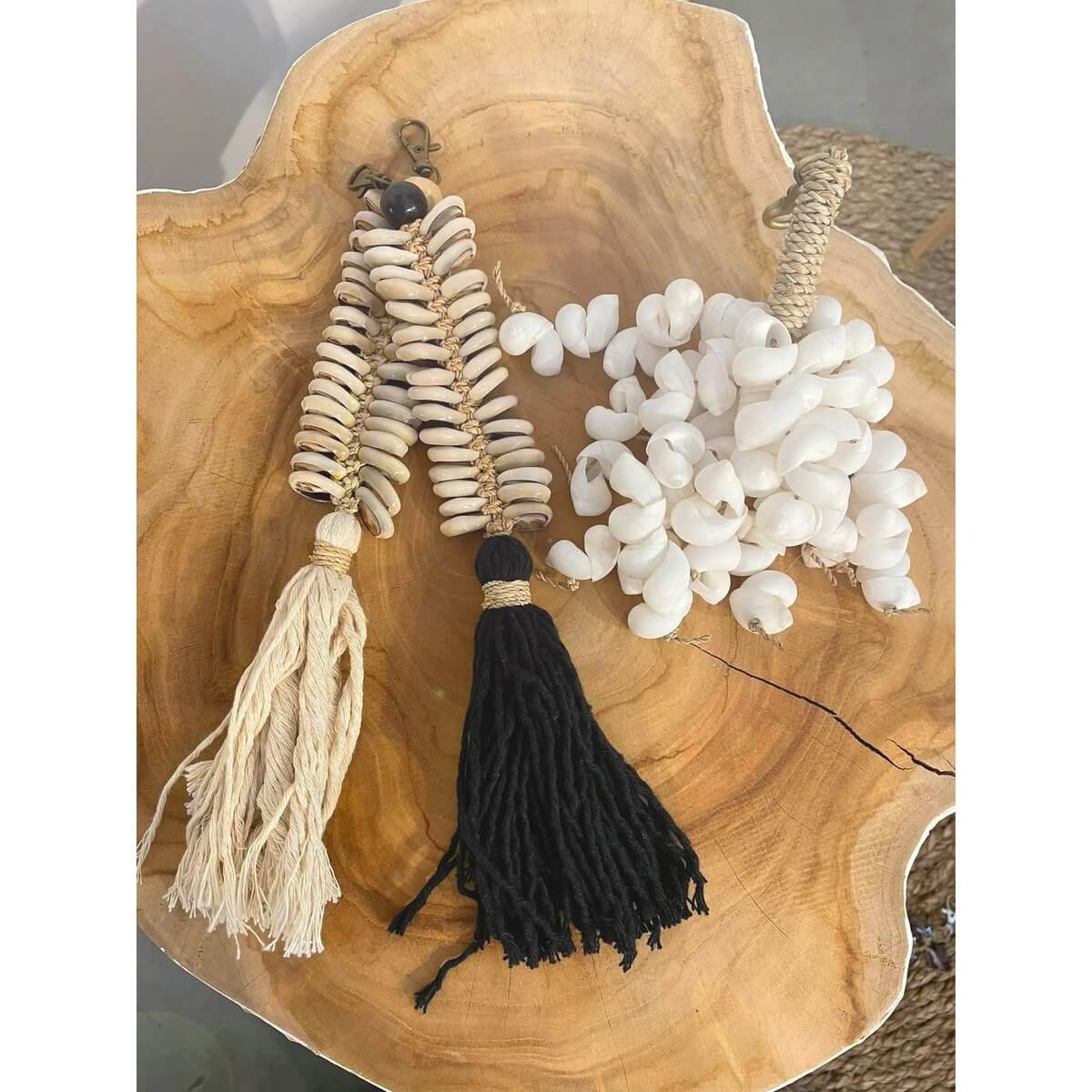 Boho-luxe macrame fishbone keychain with shells and cotton tassels, in cream and black, displayed on a wooden surface.