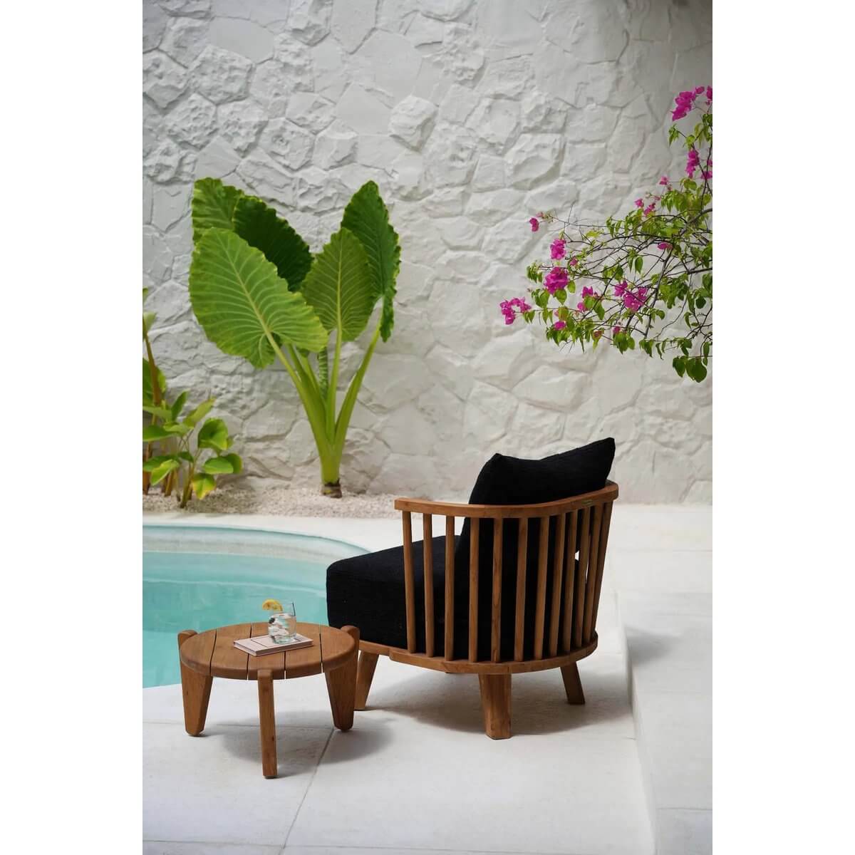 Bohemian one-seat sofa in black, crafted from reclaimed teak, with soft cushions by a poolside setting.
