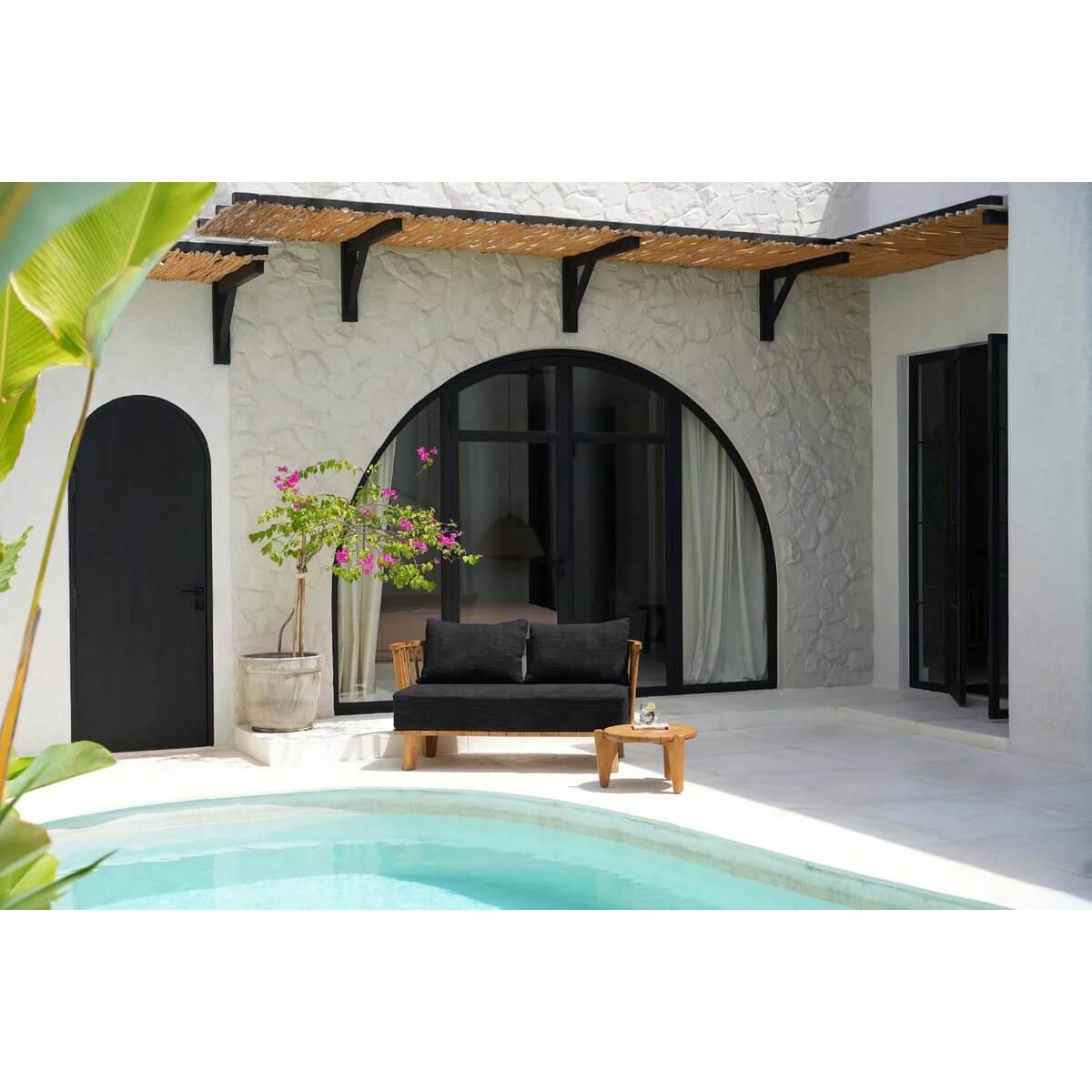 Bohemian style Malawi two-seater in natural black by the pool, made from recycled teak with soft fabric covers. Perfect for relaxing.