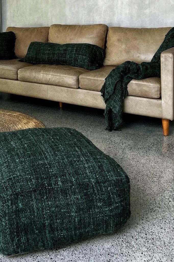 Alt Tag: Donkergroene De Oh My Gee poef bij bruine bank in stijlvolle woonkamer, handgemaakt van zacht katoen. Perfect voor indoor gebruik.