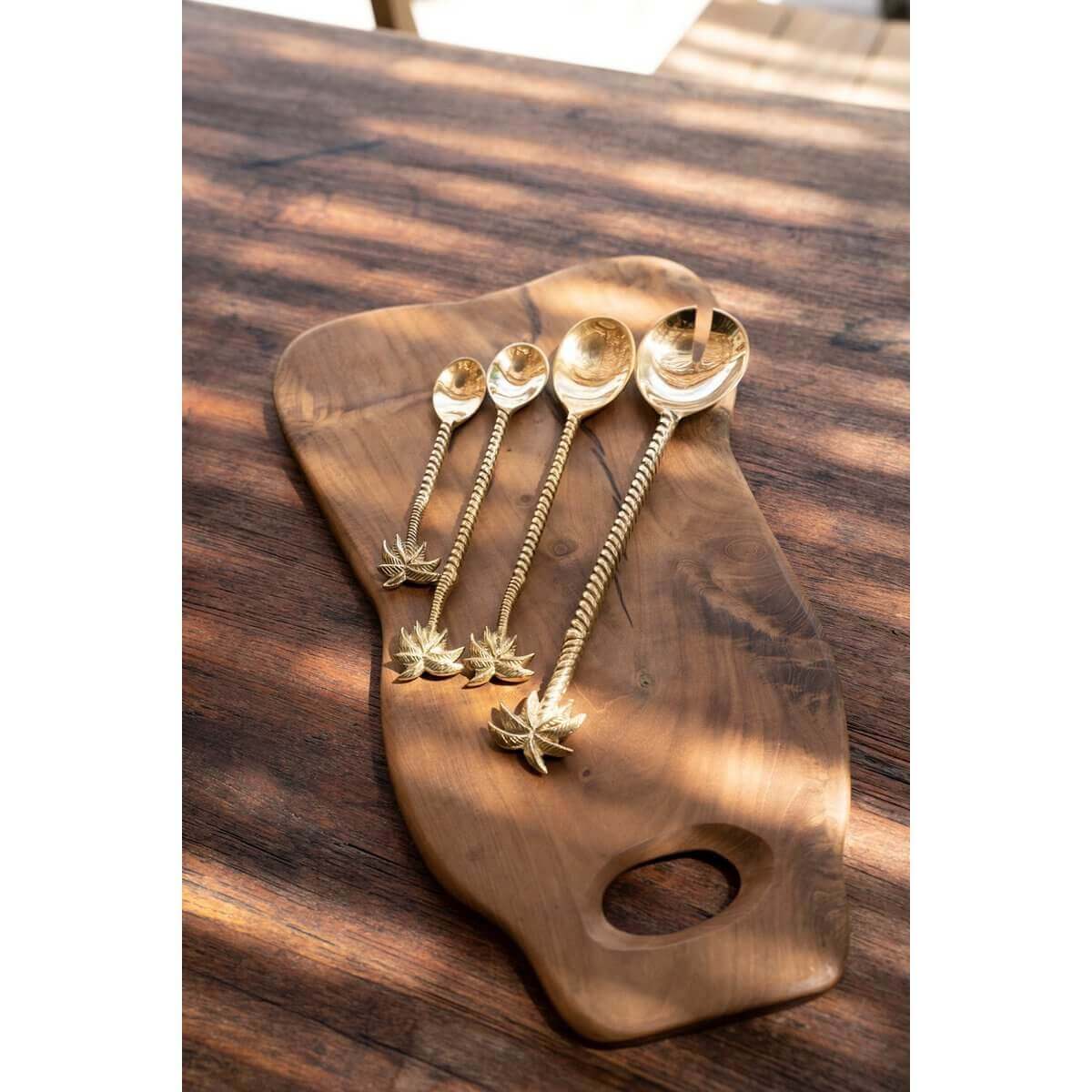 Glanzende goudkleurige vorken en lepels van messing met palmboomdetails, elegante presentatie op houten serveerplank.