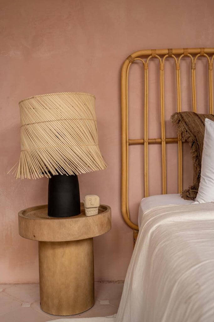De Pandan Tafellamp in zwart en naturel op houten tafel in stijlvolle slaapkamer met boho sfeer, handgeweven kap van natuurgras.
