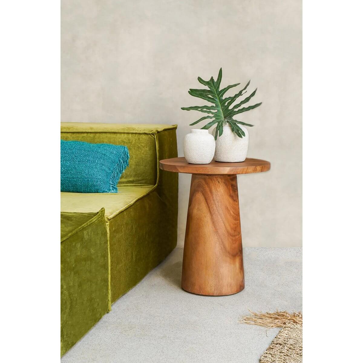 Stylish wooden side table with a Bohemian charm, adorned with two white vases and green leaves, next to a green couch.