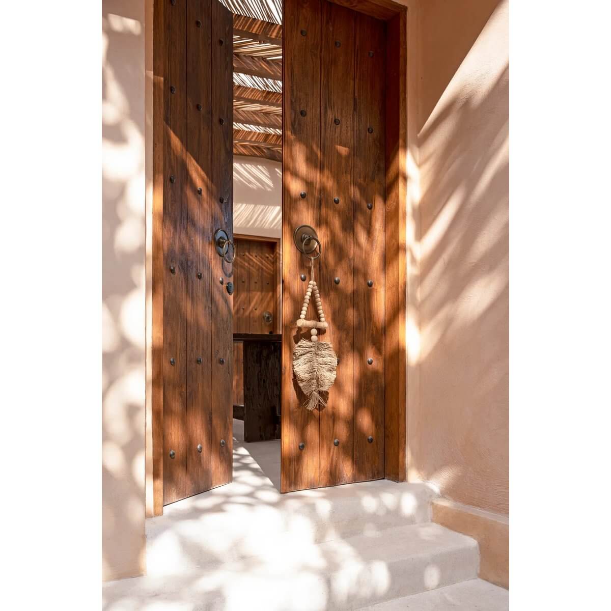 Bohemian raffia tassel decor hanging on wooden door, creating an exotic ambiance with natural sunlight patterns.