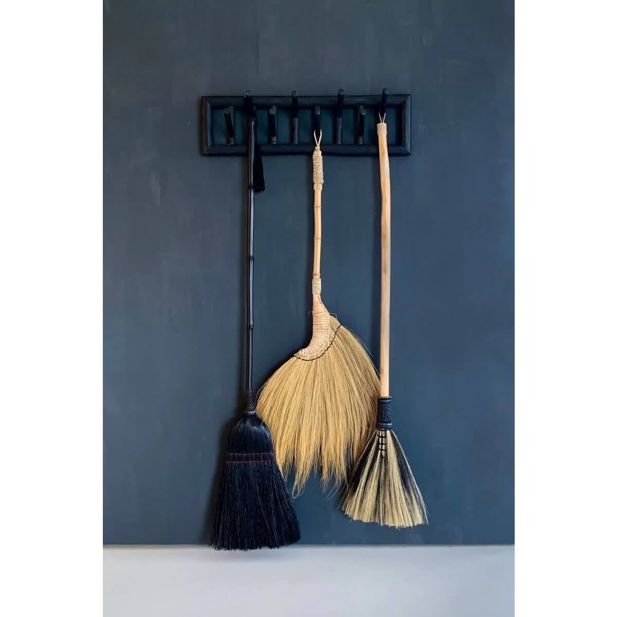 Handmade Bohemian De Rayung broom with natural fibers, perfect for interior decor, hanging against a dark wall.