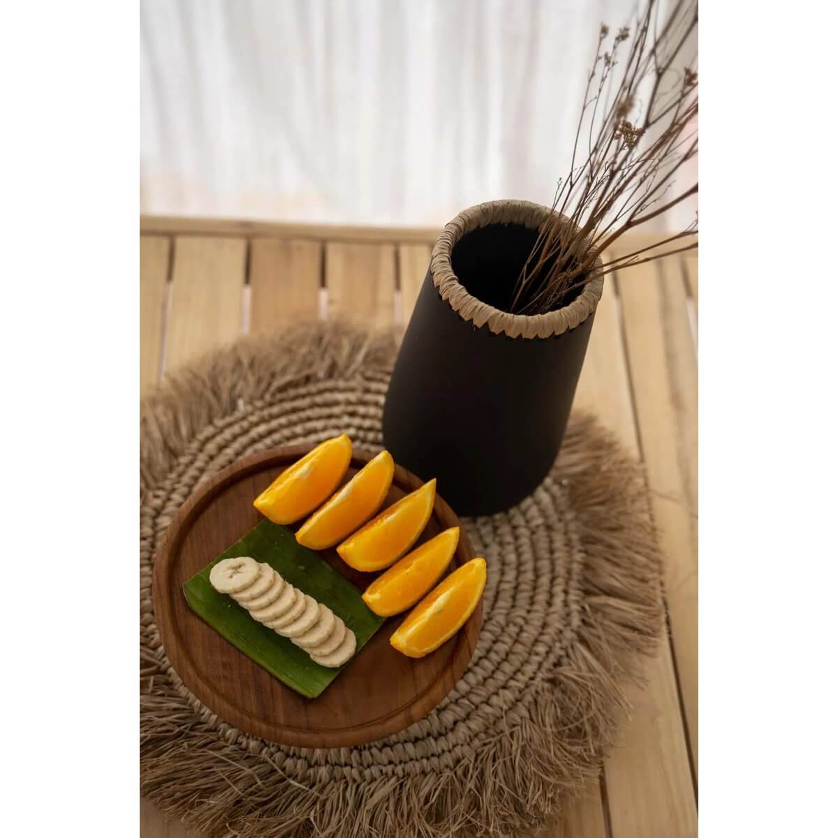 Bohemian-style table setting with a natural raffia and seagrass placemat under a vase and fruit platter.