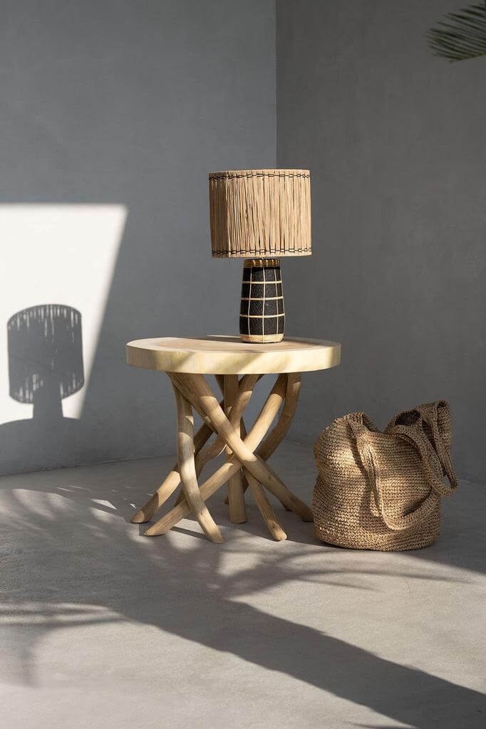 De Skiathos Tafellamp in naturel zwart, handgemaakte terracotta voet en gras kap op een stijlvol tafeltje met rieten tas. Perfect voor elke kamer.