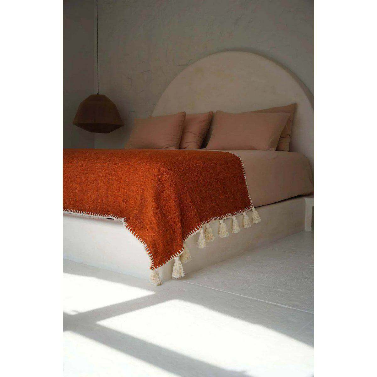 Terracotta bedsprei over een minimalistisch bed voor een warme, gezellige uitstraling in de slaapkamer.