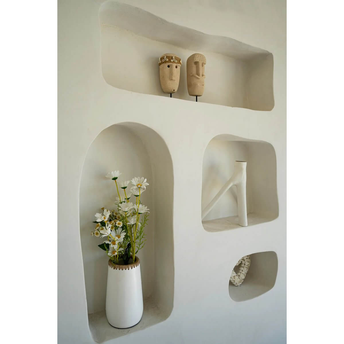 Bohemian decor with Sumba handcrafted sandstone sculptures and a vase with flowers in modern shelves.