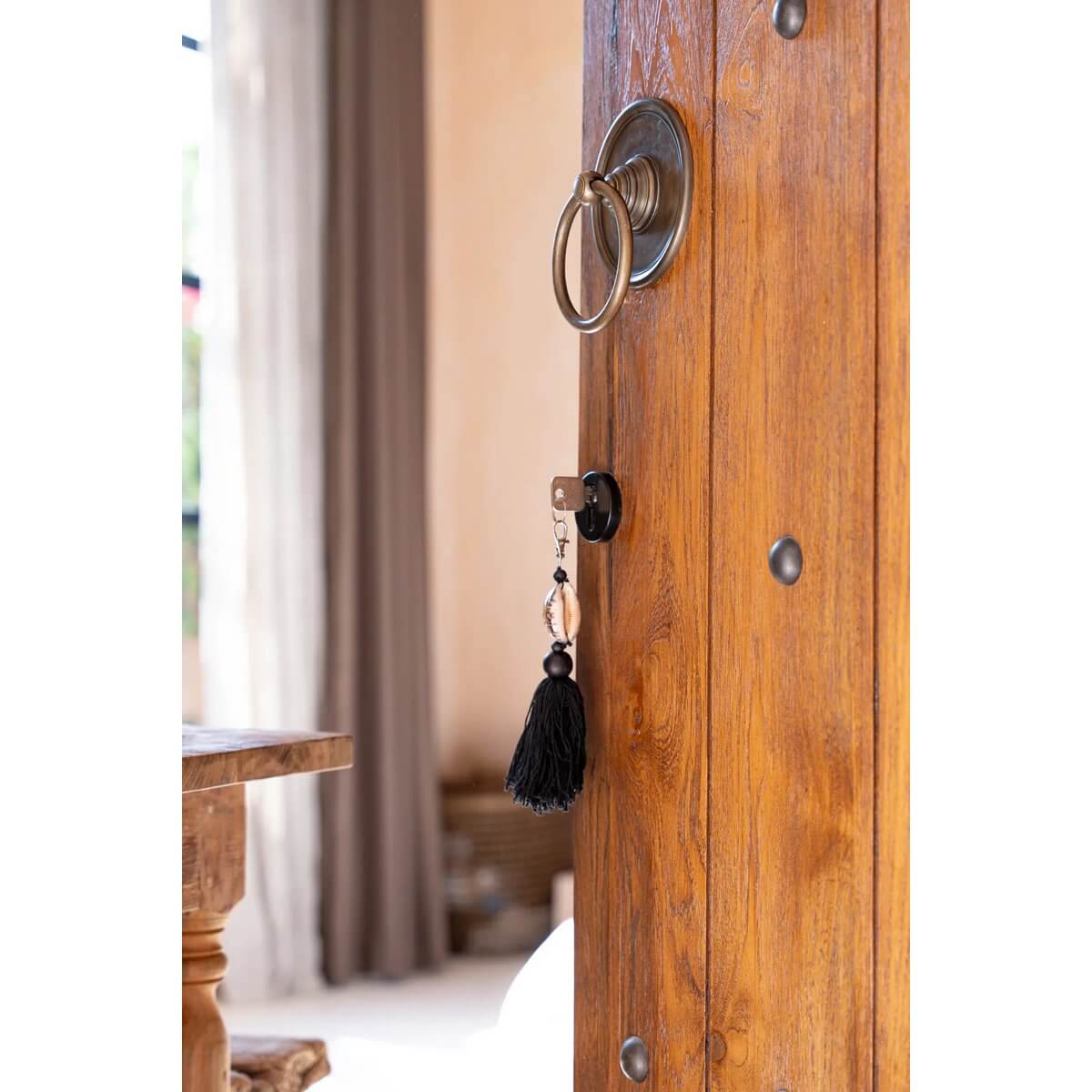 Bohemian Sumbawa keychain in black-brown with rustic charm hanging on a wooden door handle in a cozy home setting.