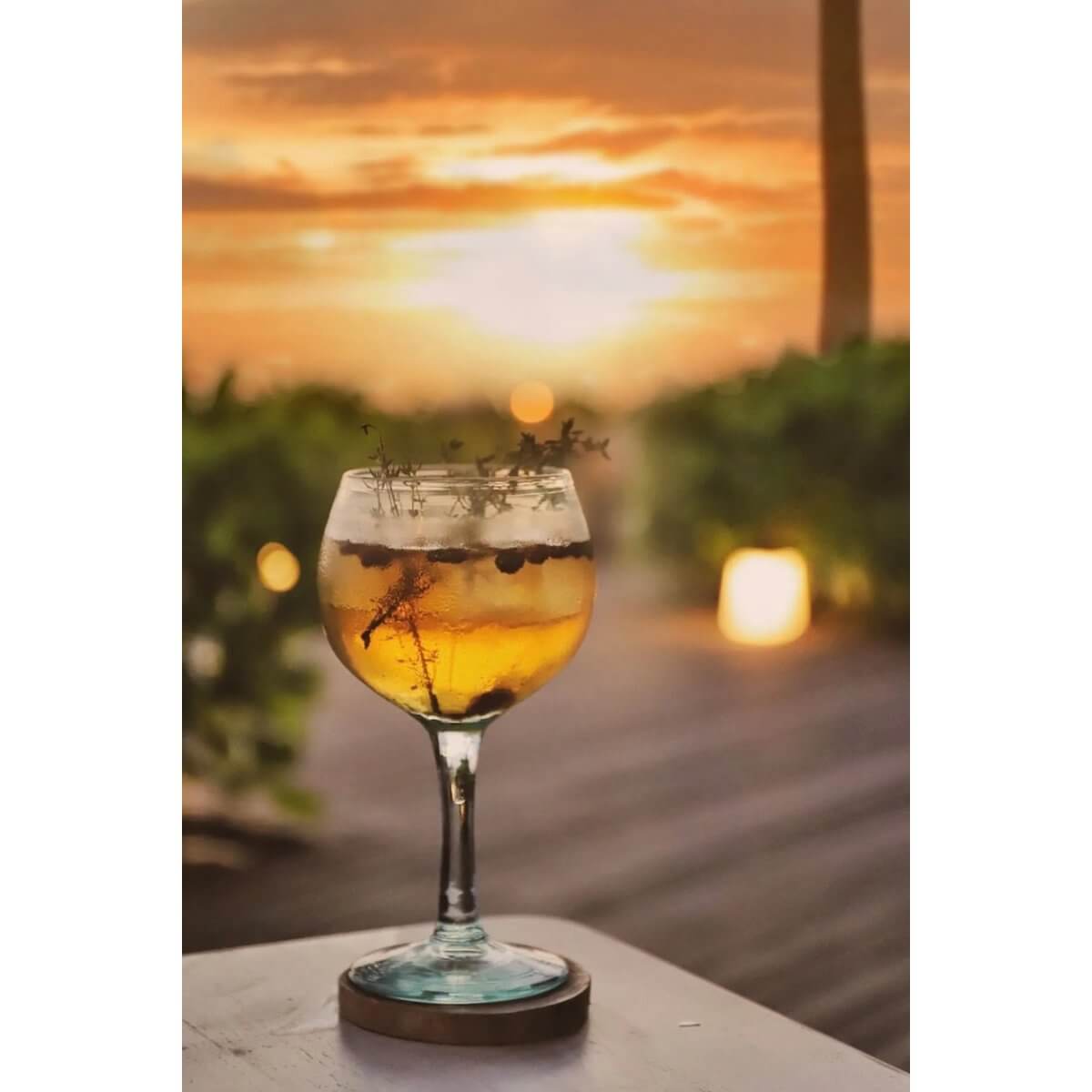 Chic cocktail on a De Teak Root Boho Coaster, set against a vibrant sunset, adding bohemian elegance to a summer evening.