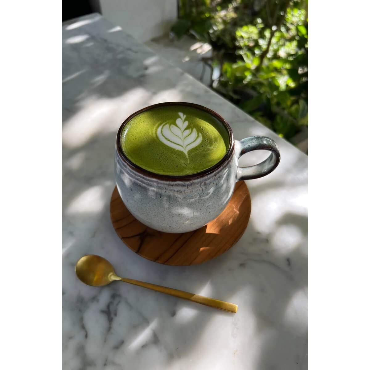 Ceramic mug with latte art on De Teak Root Nordic Coaster, next to a gold spoon, on a sunny marble table, adding Bohemian charm.