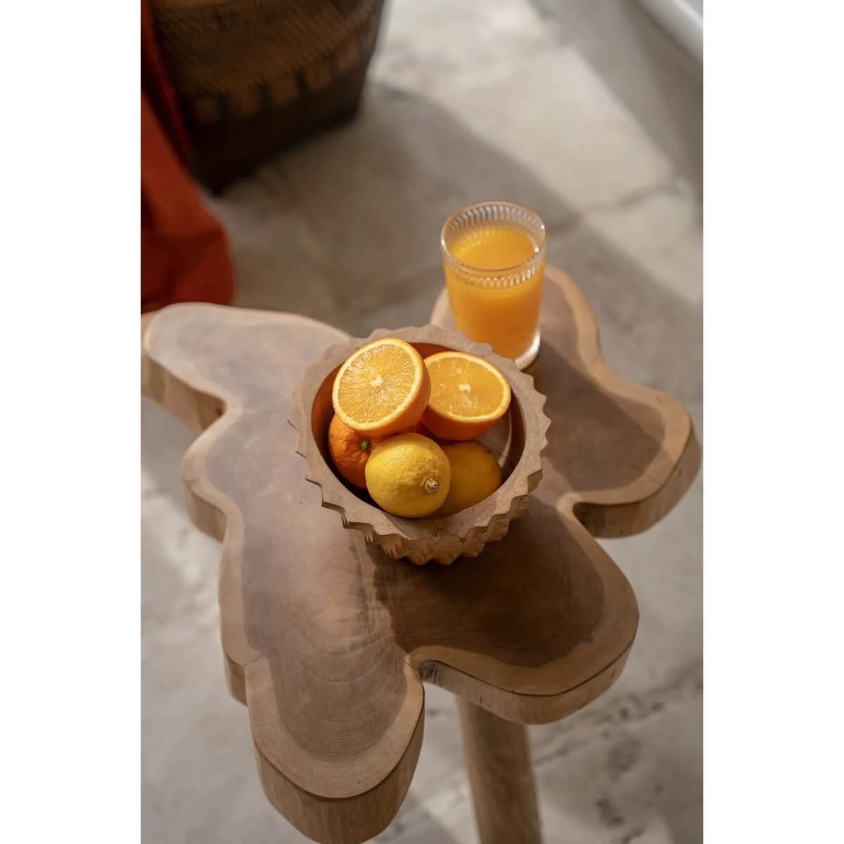 Bohemian style Durian Bowl on wooden table, filled with oranges and lemons, next to a glass of juice.