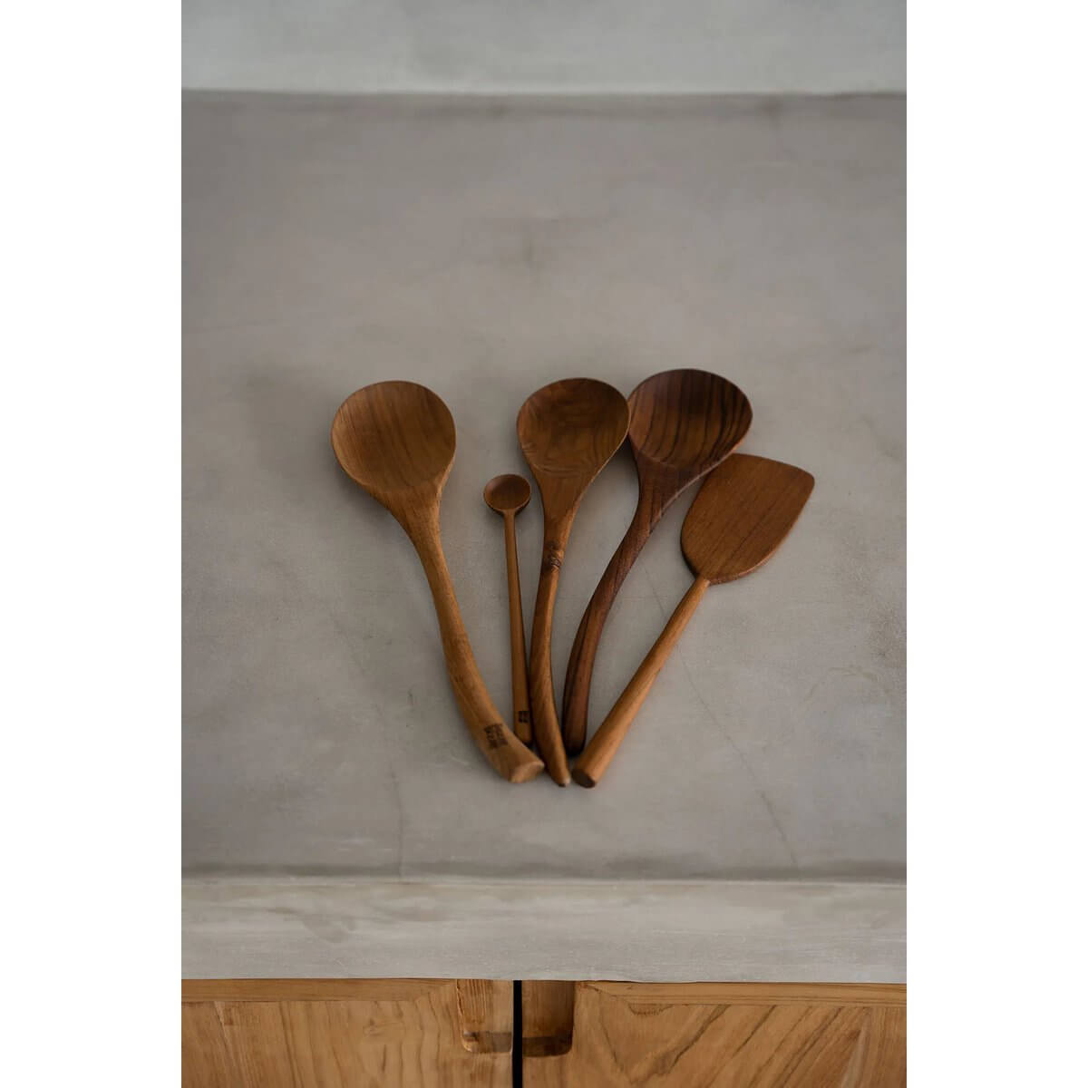 Set of wooden kitchen utensils on a countertop, featuring various spoons and spatulas made from teak, showcasing a Bohemian style.