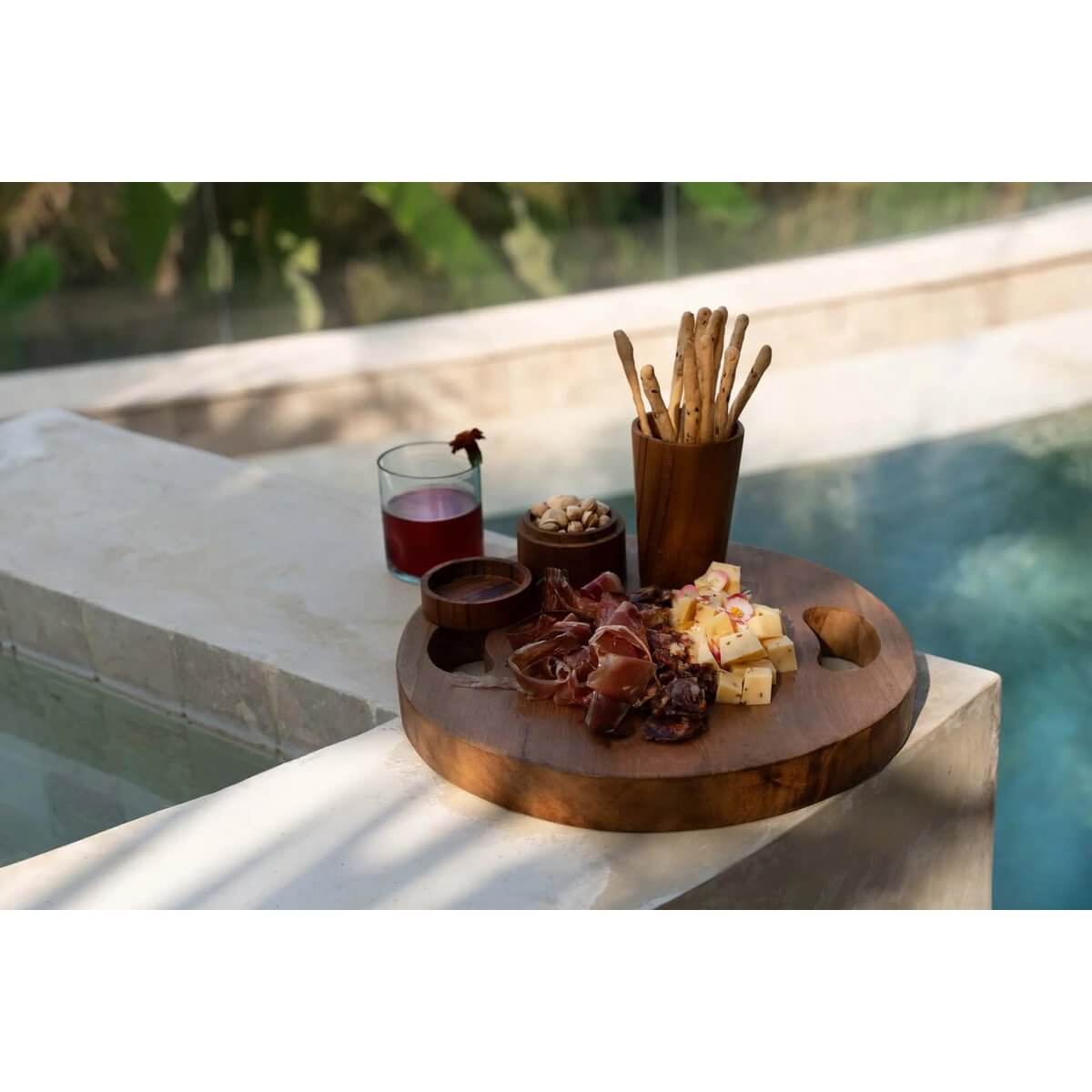 Bohemian teak root jar displayed by a pool with a selection of cheese, breadsticks, and cured meats on a wooden platter.