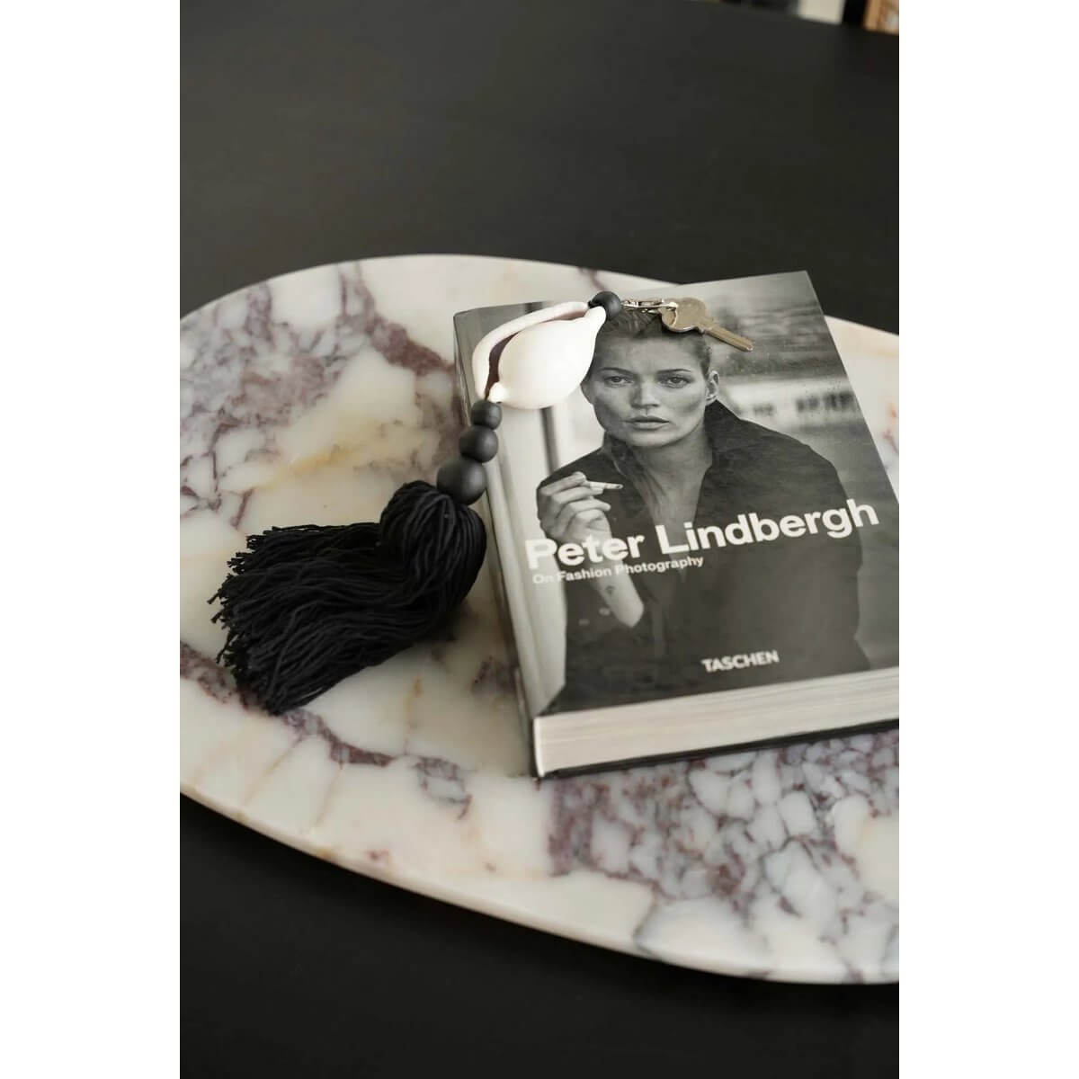 Bohemian black and white De Togian sleutelhanger on a book, made of wood and cotton, featuring a large white shell. Stylish and elegant.