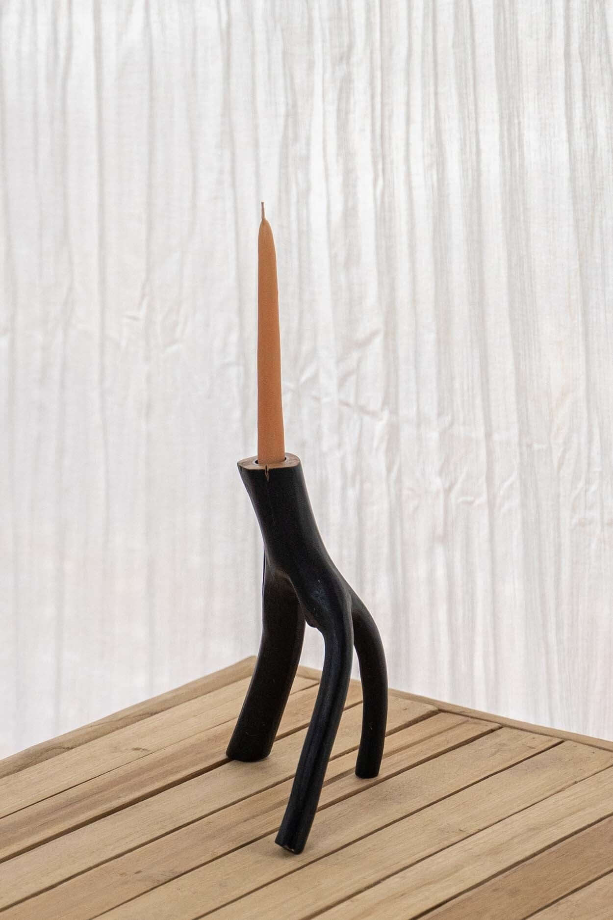 Unieke handgemaakte kaarsenhouder van donker hout met lange kaars, staand op houten tafel tegen lichte achtergrond.