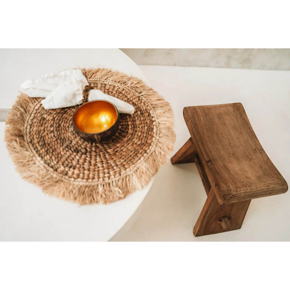 Bohemian raffia and waterhyacinth placemat in natural tones on a table, paired with a rustic wooden stool.