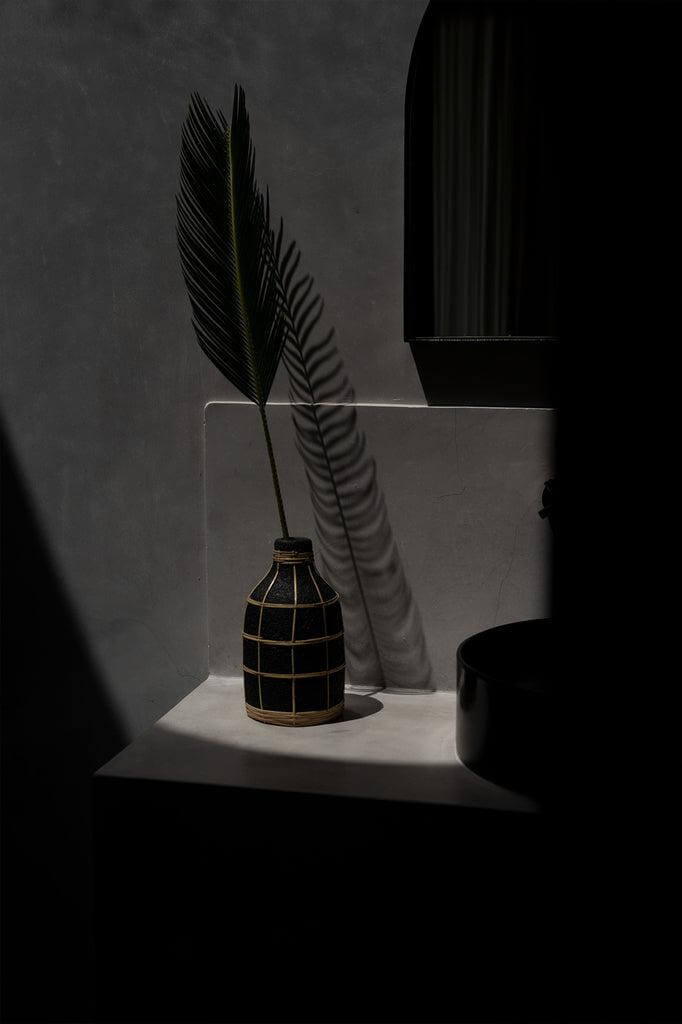 Stijlvolle De Whoopy Vaas met rotan detail, perfect voor droogbloemen, in een donkere hoek gezet, biedt een kustgevoel in elke ruimte.