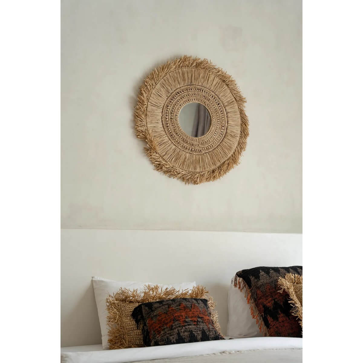 Raffia spiegeltje met natuurlijke franjes hangt boven een bed in een modern interieur.