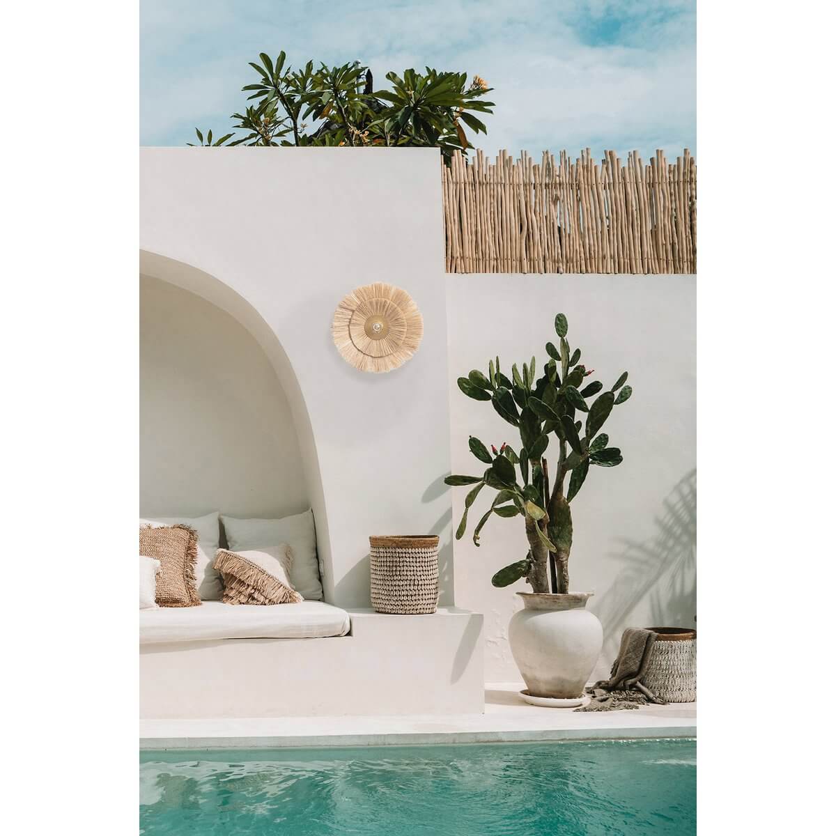 Bohemian outdoor lounge with white arch, woven decor, cacti, and poolside bliss under a blue sky.