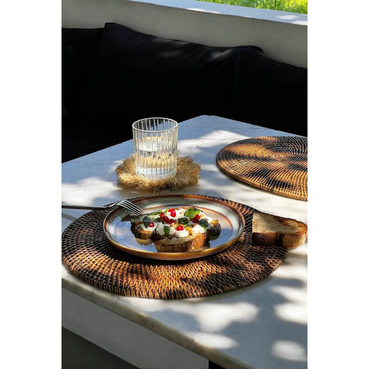 Bohemian table setting with Bazar Bizar Living colonial placemat in natural brown, featuring a plate of bruschetta and a glass of water.