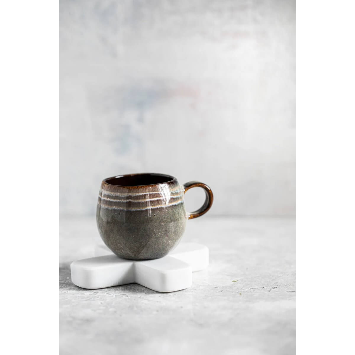 Bohemian style gray mug on a white marble trivet by Bazar Bizar Living, perfect for adding elegance to any table setting.
