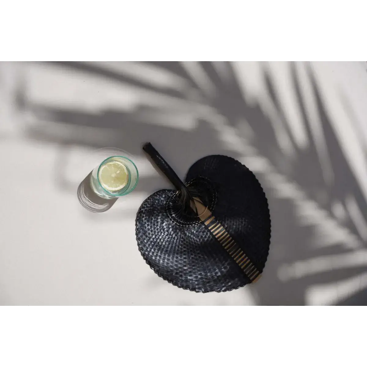 Bohemian recycled glass with lime beside stylish black hand fan casting palm shadows