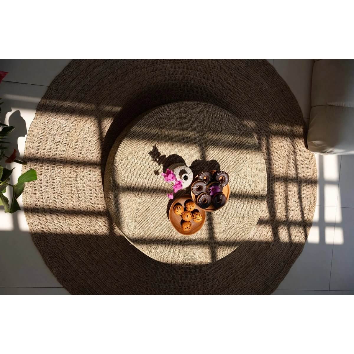Bohemian-style living room with a round rattan rug and assorted decorative items casting artistic shadows in warm sunlight.