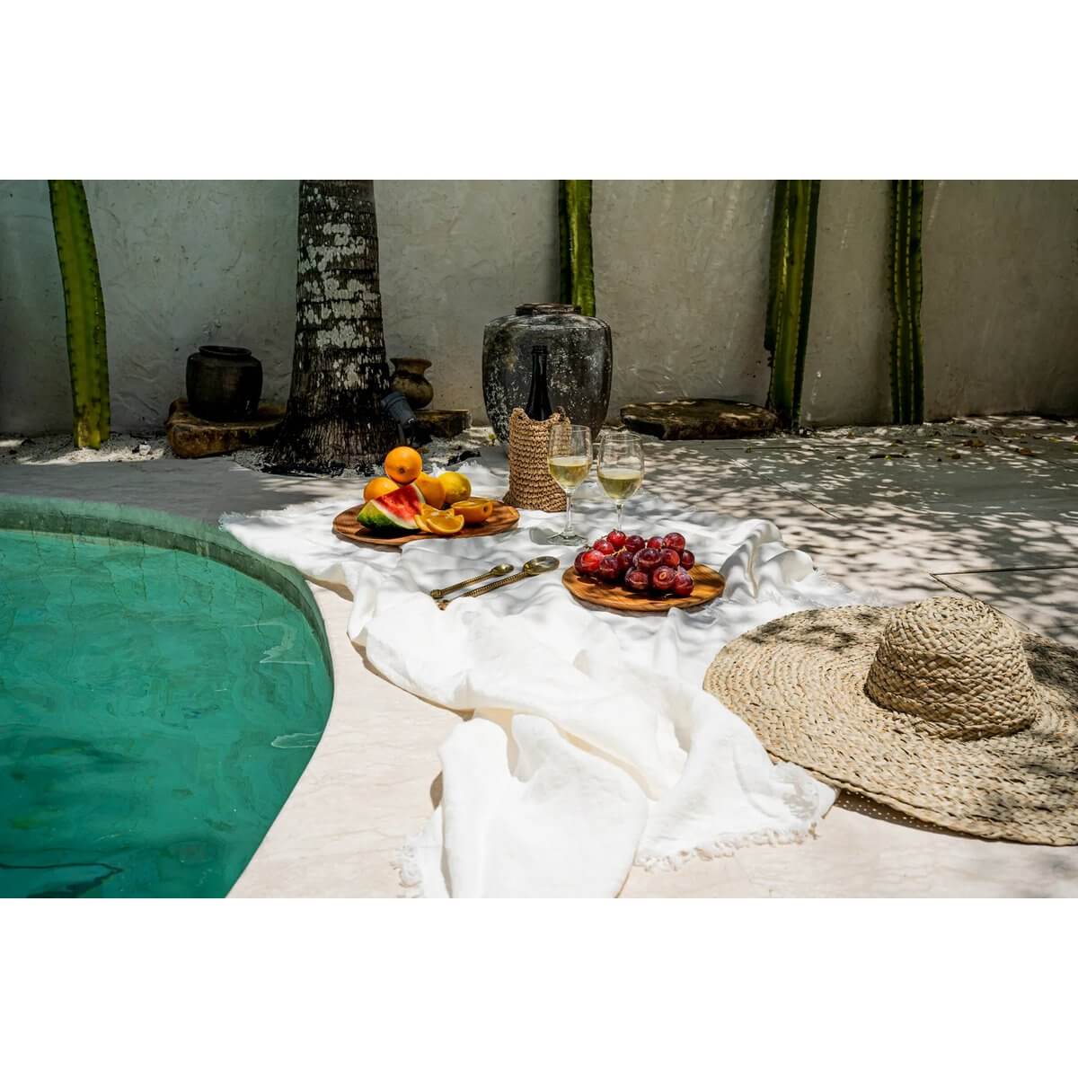 Ontspannen picknick bij het zwembad met wit linnen tafelkleed, fruit, wijn en zonnehoed in de zon.