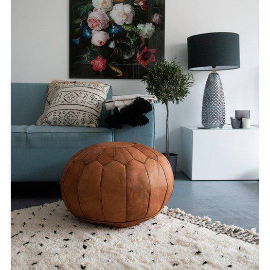Cognacbruine leren poef in een gezellige woonkamer, perfect voor boho stijl en multifunctioneel gebruik als voetenbankje of zitplaats.