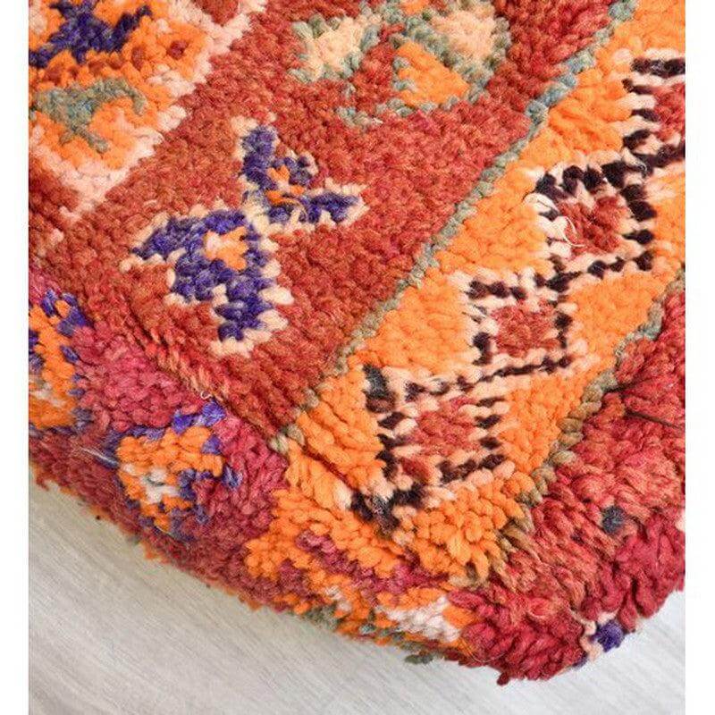 Close-up van kleurrijk Marokkaans vloerkussen met vintage Berberpatroon in rode en oranje tinten, bohemian interieurdecoratie.