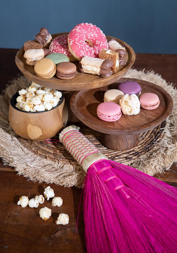 Houten schaal met macarons en snacks op raffia placemat met roze decoratief stuk.