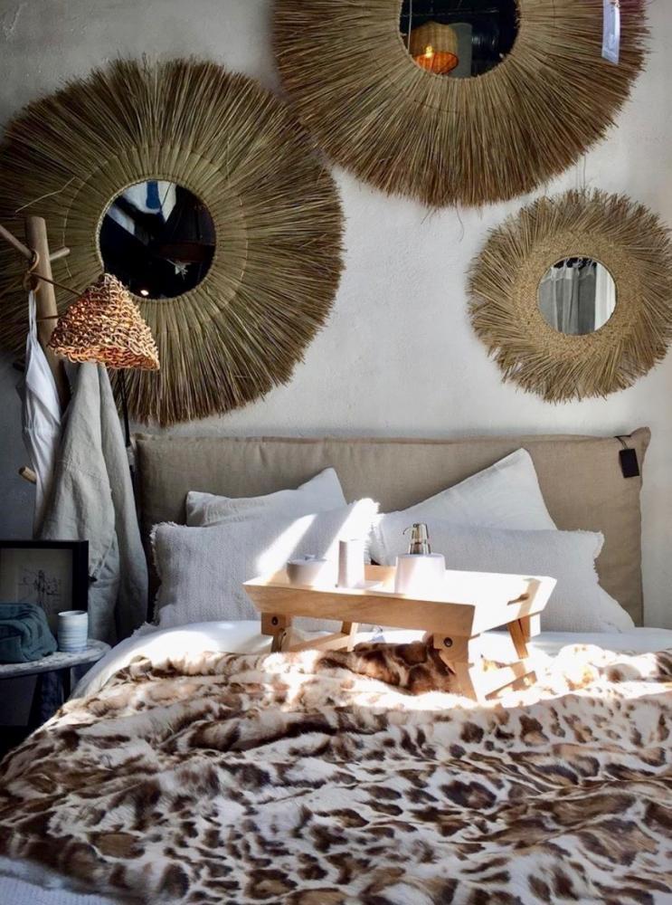 Ronde rotan spiegel lux aan de muur in boho slaapkamer; handgemaakte decoratie voor meer sfeer en diepte.