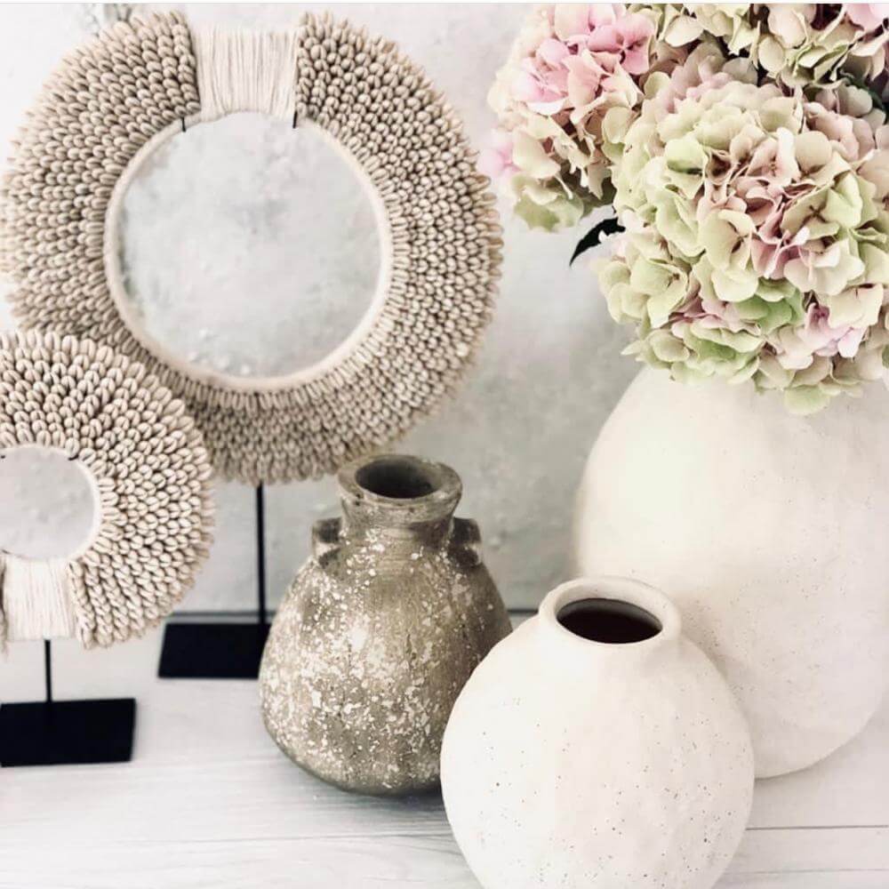 Decoratieve schelpenketting op standaard met vazen en bloemen, perfect voor een Ibiza woonkamer met ontspannen sfeer.